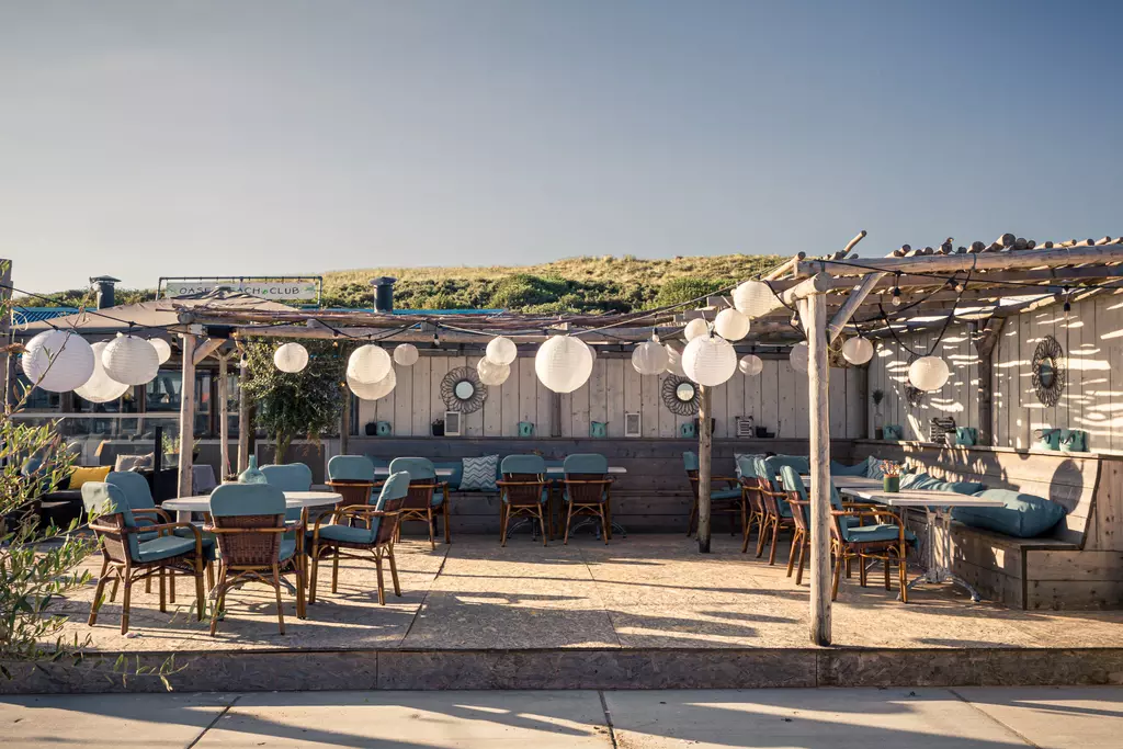 Wooden terrace with tables and chairs, surrounded by hanging lanterns and comfortable seating areas.