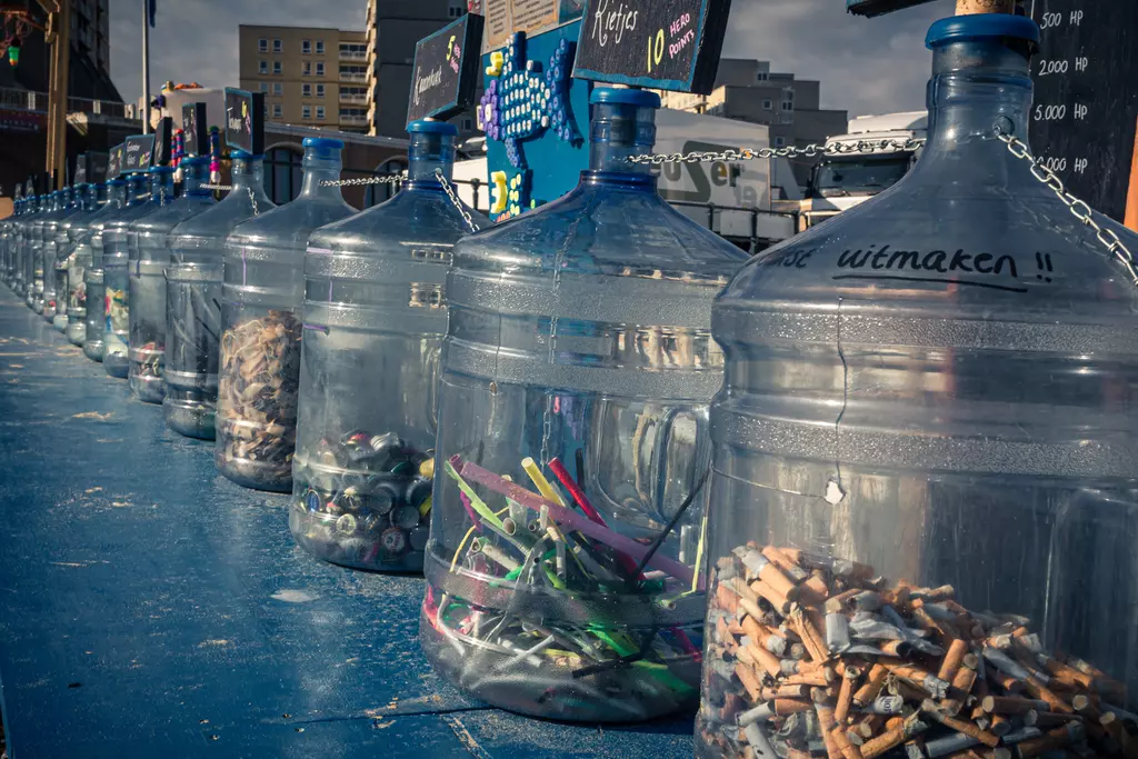 Transparent containers are lined up on a blue table, filled with various colorful materials and recycling items.