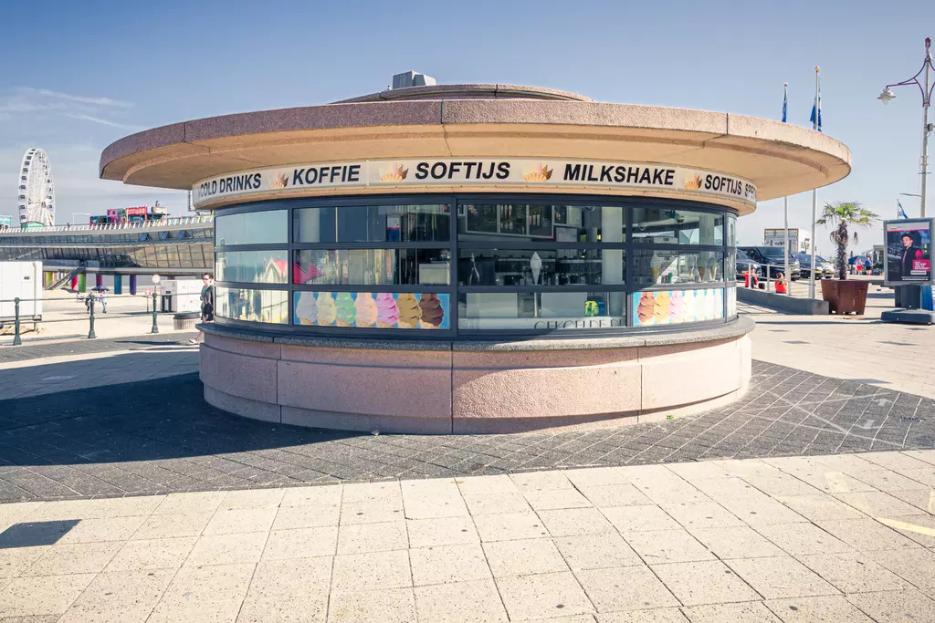 A round kiosk with large windows offering various food and drinks, surrounded by paved walkways.