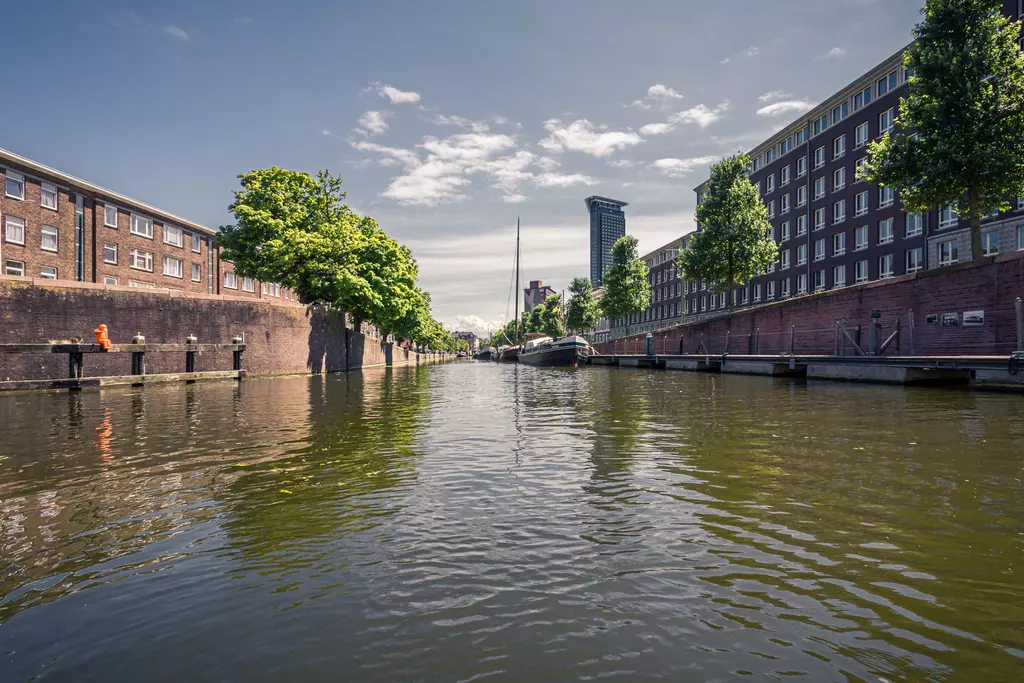 A serene waterway between buildings and trees, with a boat in the canal and a clear sky above.