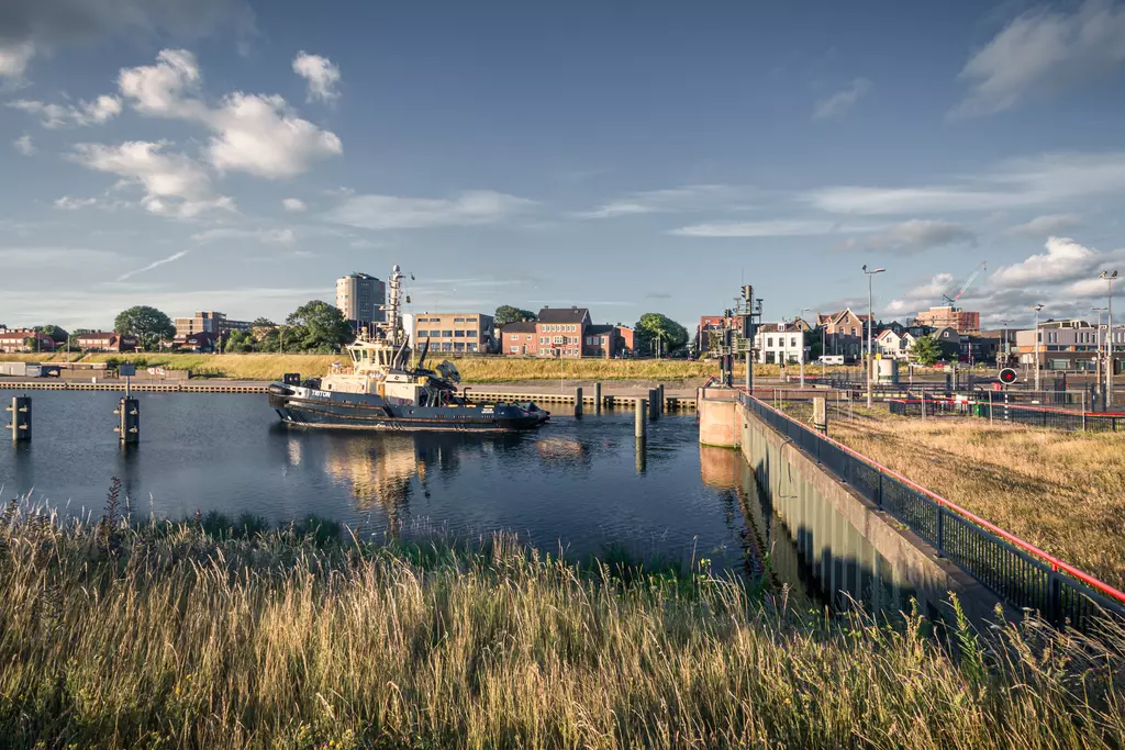 A harbor with a tugboat, surrounded by grass and city buildings in the background.