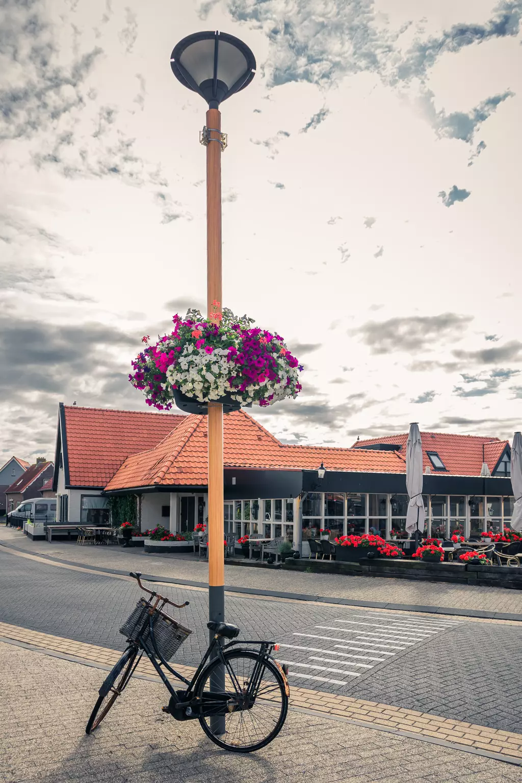 Fahrrad in Callantsoog: Ein schwarzes Fahrrad lehnt an einem Laternenpfahl, dekoriert mit bunten Blumen, im Hintergrund ein Restaurant.