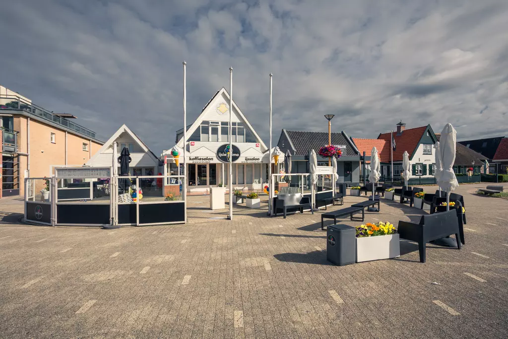 Callantsoog: Das Bild zeigt ein modernes Gebäude mit Sitzgelegenheiten und Blumenkästen auf einem Platz.