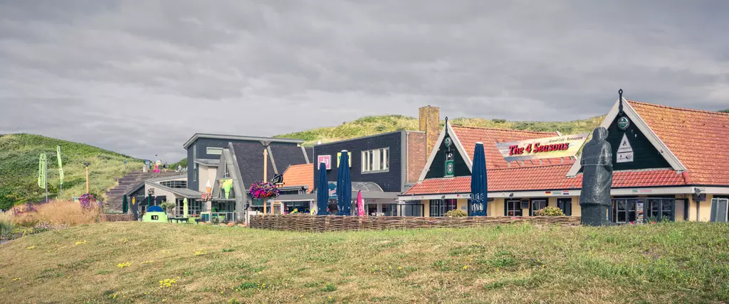 Callantsoog: Farbenfrohe Gebäude in einem Küstendorf, umgeben von Dünen und grünem Gras, mit einigen Sonnenschirmen.