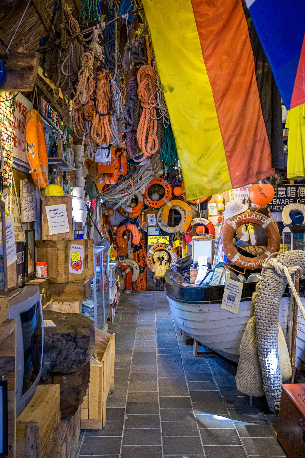 Strandmuseum auf Texel: Ein schmaler Innenraum voller Seile, Rettungsringe, Flaggen und Booten, die maritime Erinnerungen zeigen.