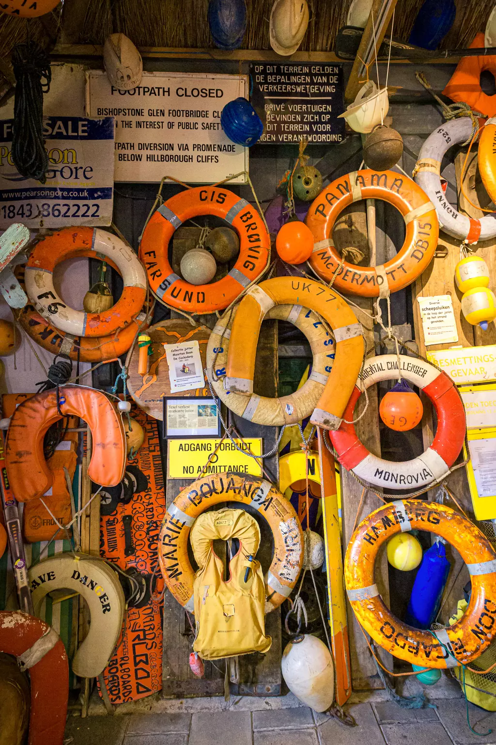 Rettungsringe in Texel: Eine Wand voller bunter Rettungsringe und Schilder, die Sicherheitshinweise geben und den Raum gestalten.