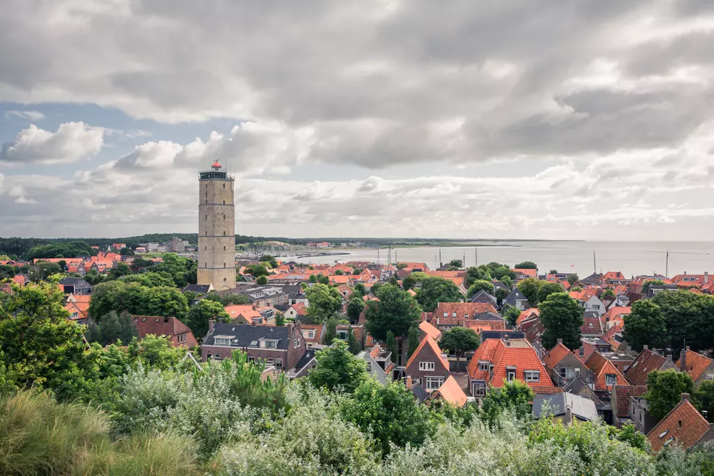 Leuchtturm auf Terschelling: Ein Blick auf eine malerische Küstenstadt, mit orangefarbenen Dächern und einem hohen Leuchtturm.