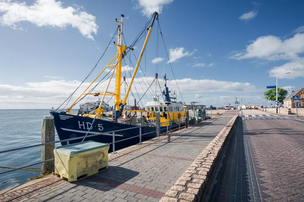 Terschelling: Fischereiboot liegt an einem Kai, umgeben von Wellen und einem gepflasterten Gehweg.