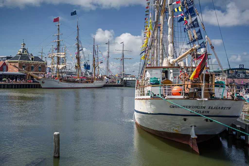 Ships in the harbor of Harlingen: Two magnificent sailing vessels docked in the harbor, surrounded by colorful flags and a picturesque backdrop.