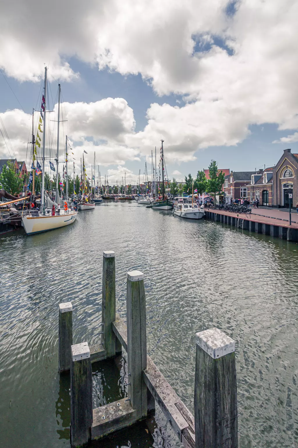 Harlingen harbor: A tranquil waterway lined with sailing boats and a wooden jetty, surrounded by trees and historic buildings.