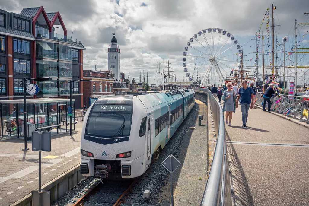 Train station in Harlingen: A train stops on tracks near a harbor, surrounded by modern buildings and a ferris wheel.