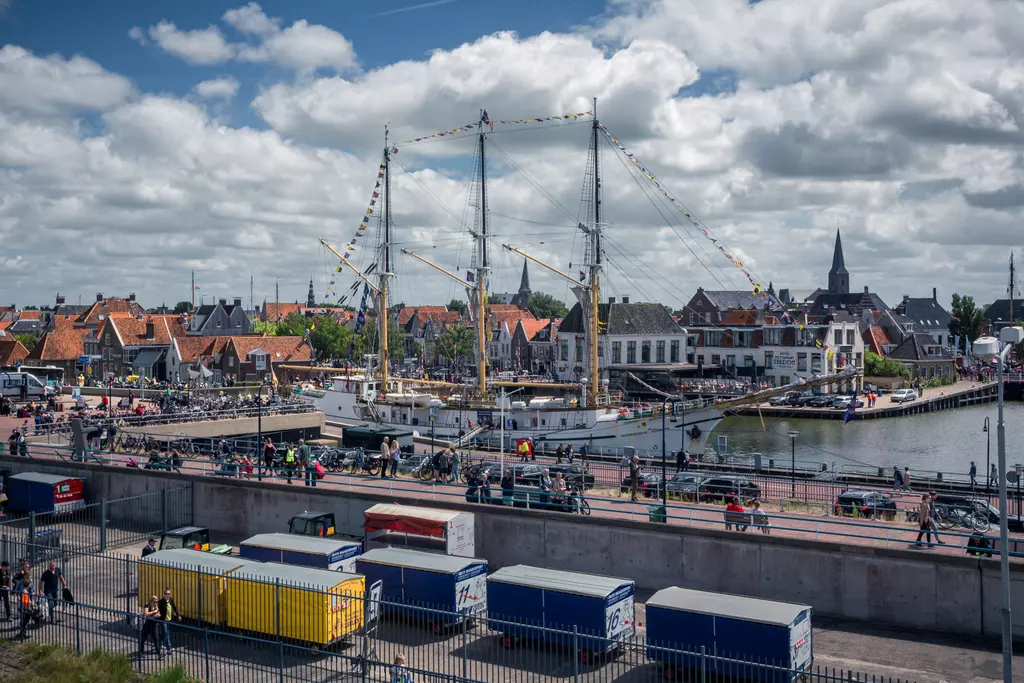 Harbor in Harlingen: A ship with masts and colorful flags is docked, surrounded by historic buildings and crowds of people.