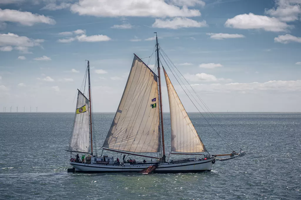 Sailing ship in Harlingen: A classic sailboat with billowing sails glides over the water, with wind turbines visible in the background.