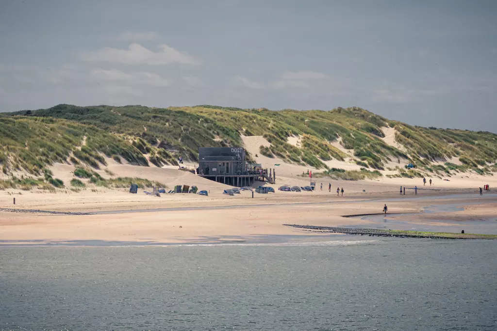 Beach on Vlieland: A vast sandy area with dunes in the background and a small building on the shore, people strolling around.