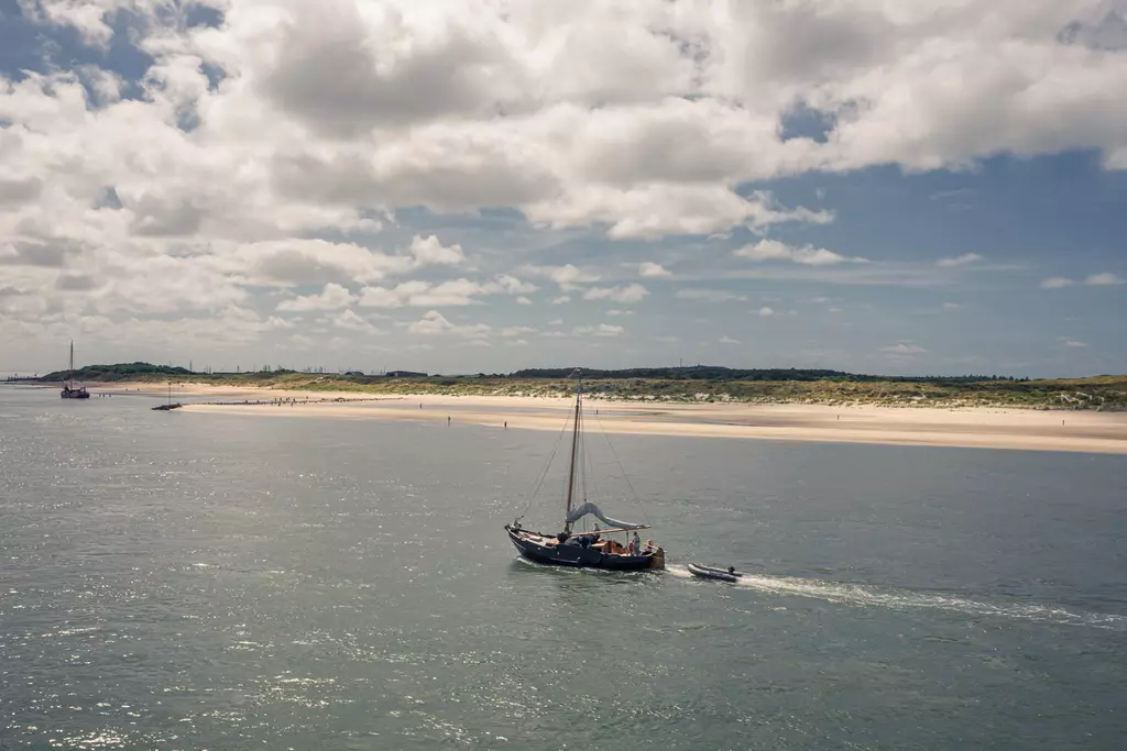 A boat sails over calm waters, with sandy beaches and gentle hills visible in the background.