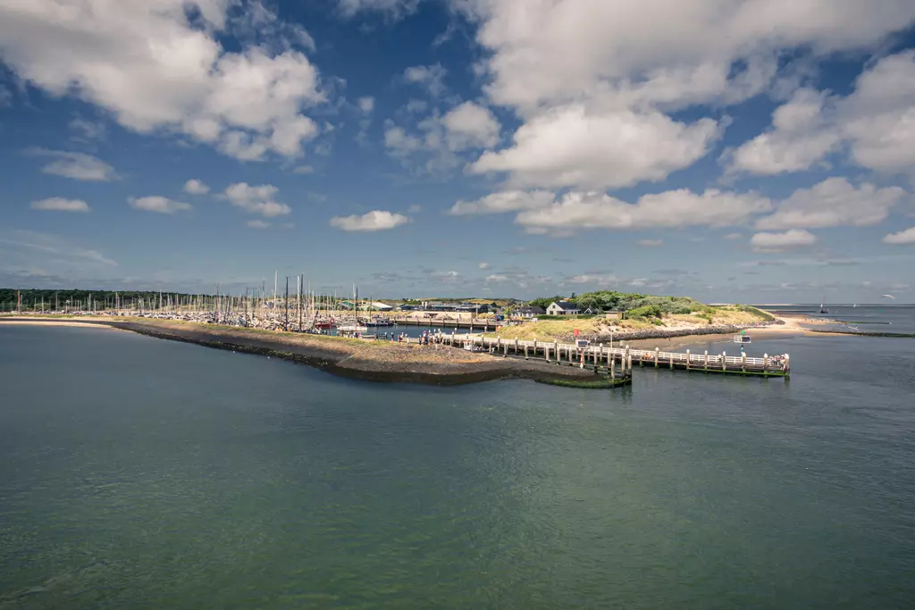 Pier in Vlieland: A wooden platform extends into the water, surrounded by boats and a green island in the background.