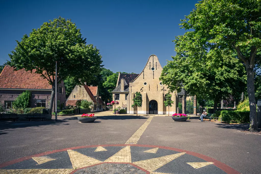 Vlieland: A historic square featuring a distinctive church, surrounded by green trees and charming buildings.