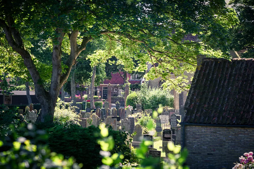 Cemetery in Vlieland: A tranquil scene with gravestones among green trees and a modern building in the background.