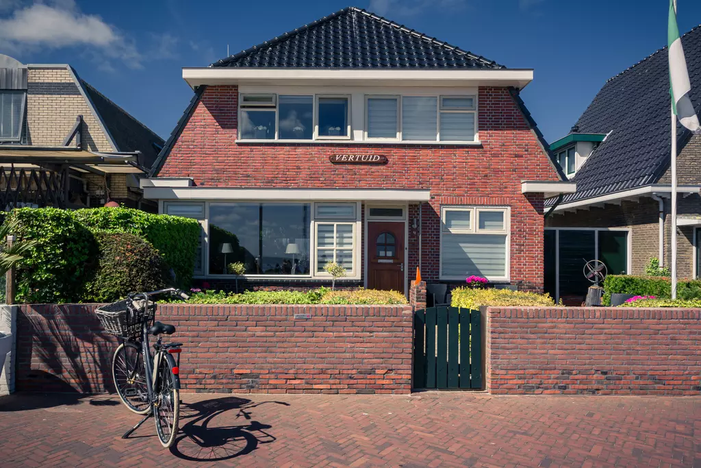 House in Vlieland: Red brick facade with large windows, green hedge, and a bicycle in front of the entrance door.