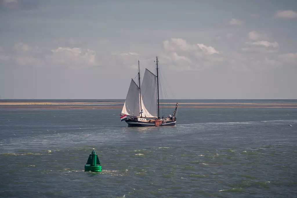 Sailing boat off Vlieland: A traditional sailboat with large white sails glides across a calm water surface.