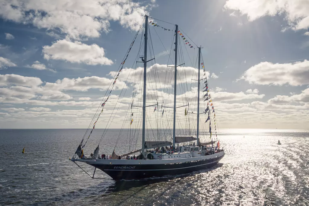 Sailing ship in Harlingen: A tall ship adorned with colorful flags glides across the water, surrounded by a clear sky and clouds.