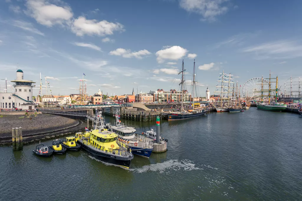 Harbor in Harlingen: Several boats are in the water, historic ships docked at the quay, with colorful buildings of the town in the background.