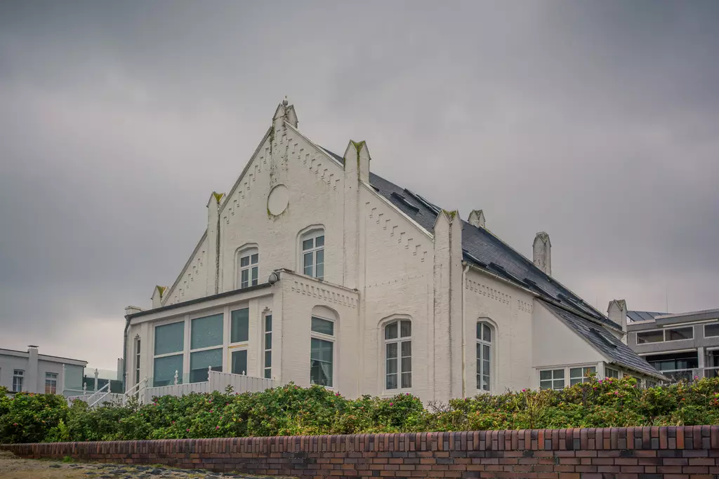 Ein elegantes, weißes Gebäude mit spitzen Dächern und einem hohen Giebel, umgeben von einer gepflegten grünen Hecke.