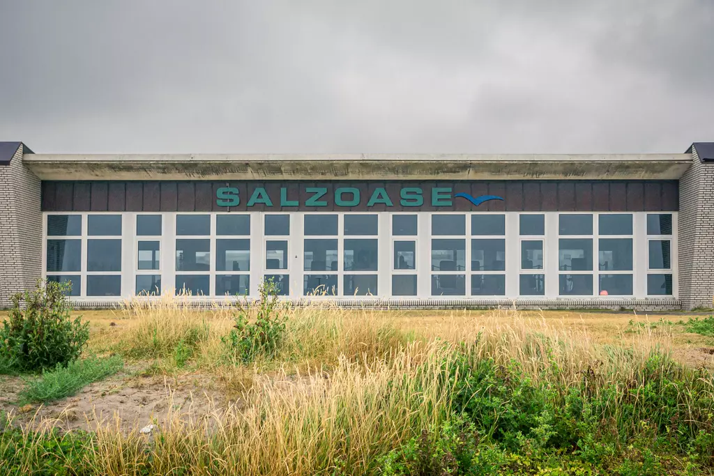 Eine moderne, flache Gebäudeoberfläche mit großen Fenstern und der Aufschrift Salzoase in grünen Buchstaben, umgeben von Gras.