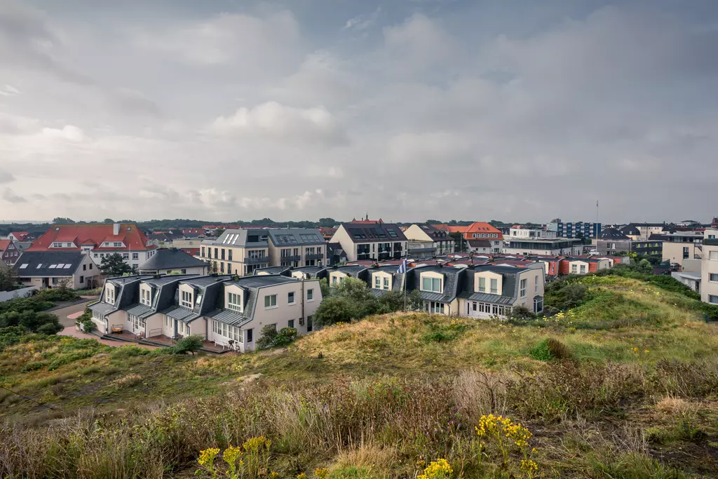 Eine Aussicht auf die Stadt Norderney mit modernen Häusern und einer bewachsenen Dünenlandschaft im Vordergrund.