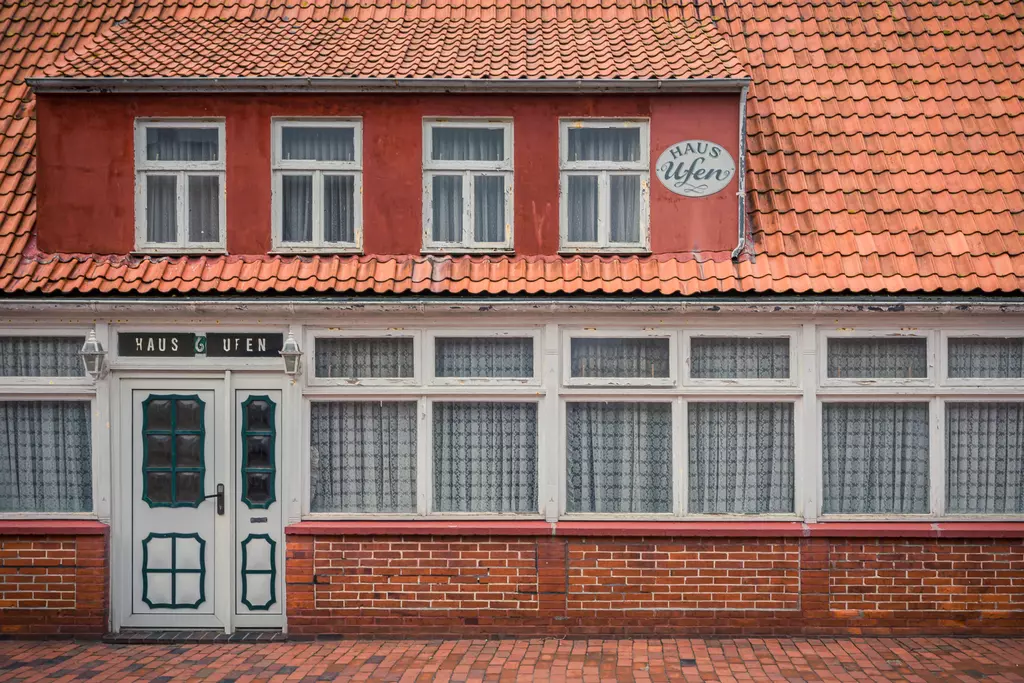 Ein rotes Haus mit verzierten Fenstern und einem großen, grünen Eingangstür. Ziegelsteine und Dachziegel sind sichtbar.