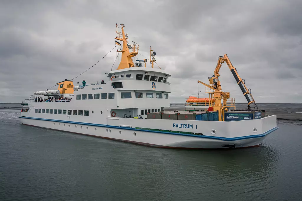 A large ship with an orange superstructure is docked in the harbor, surrounded by gray water and a cloudy sky.