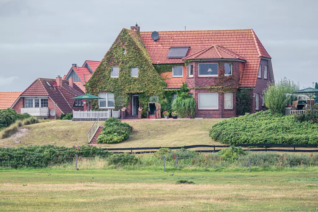 A two-story red brick house with a sloping roof, surrounded by lush greenery and a well-kept garden.