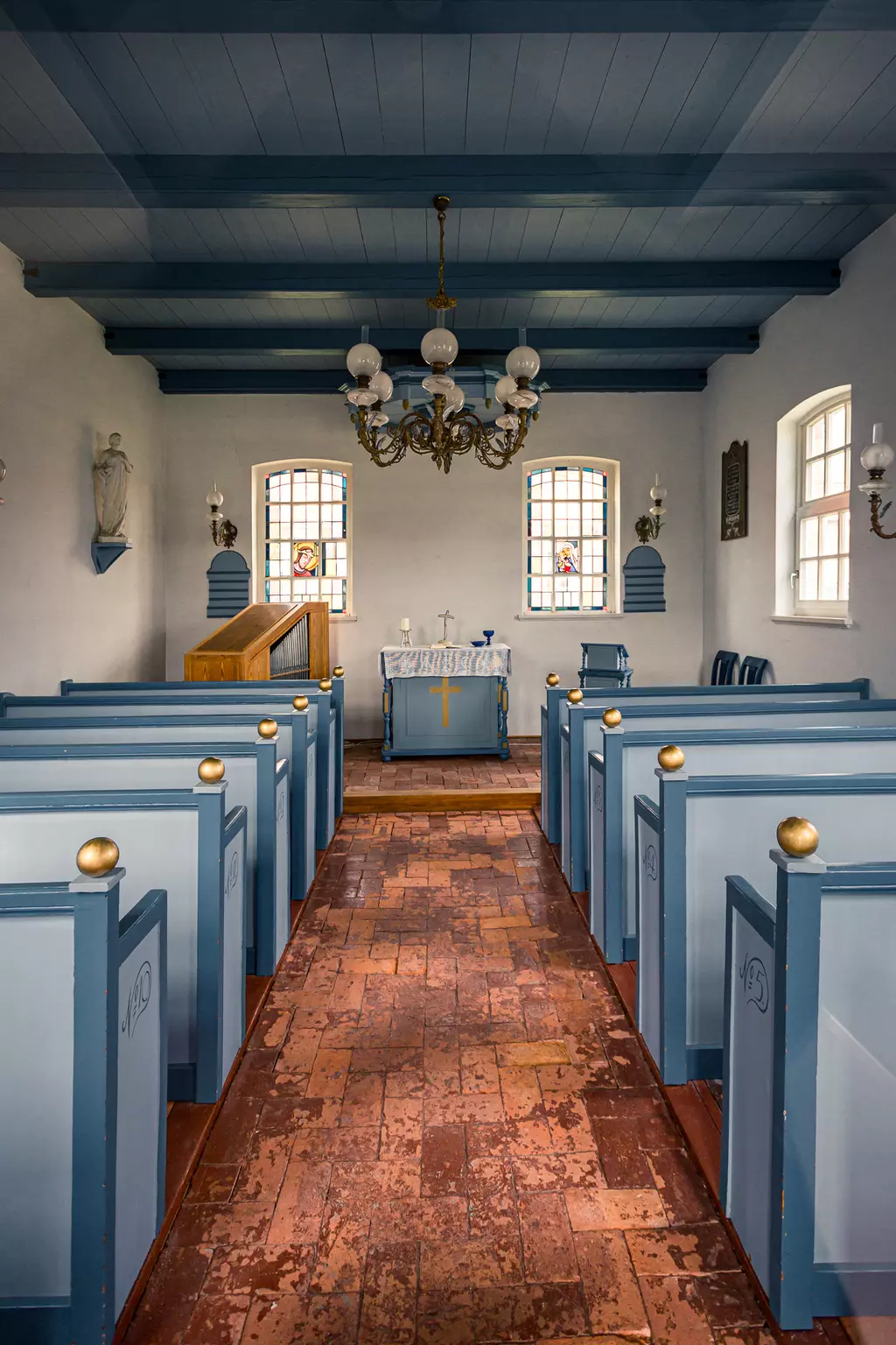 View of the church interior with blue pews, an altar in the center, and a chandelier hanging from the ceiling.