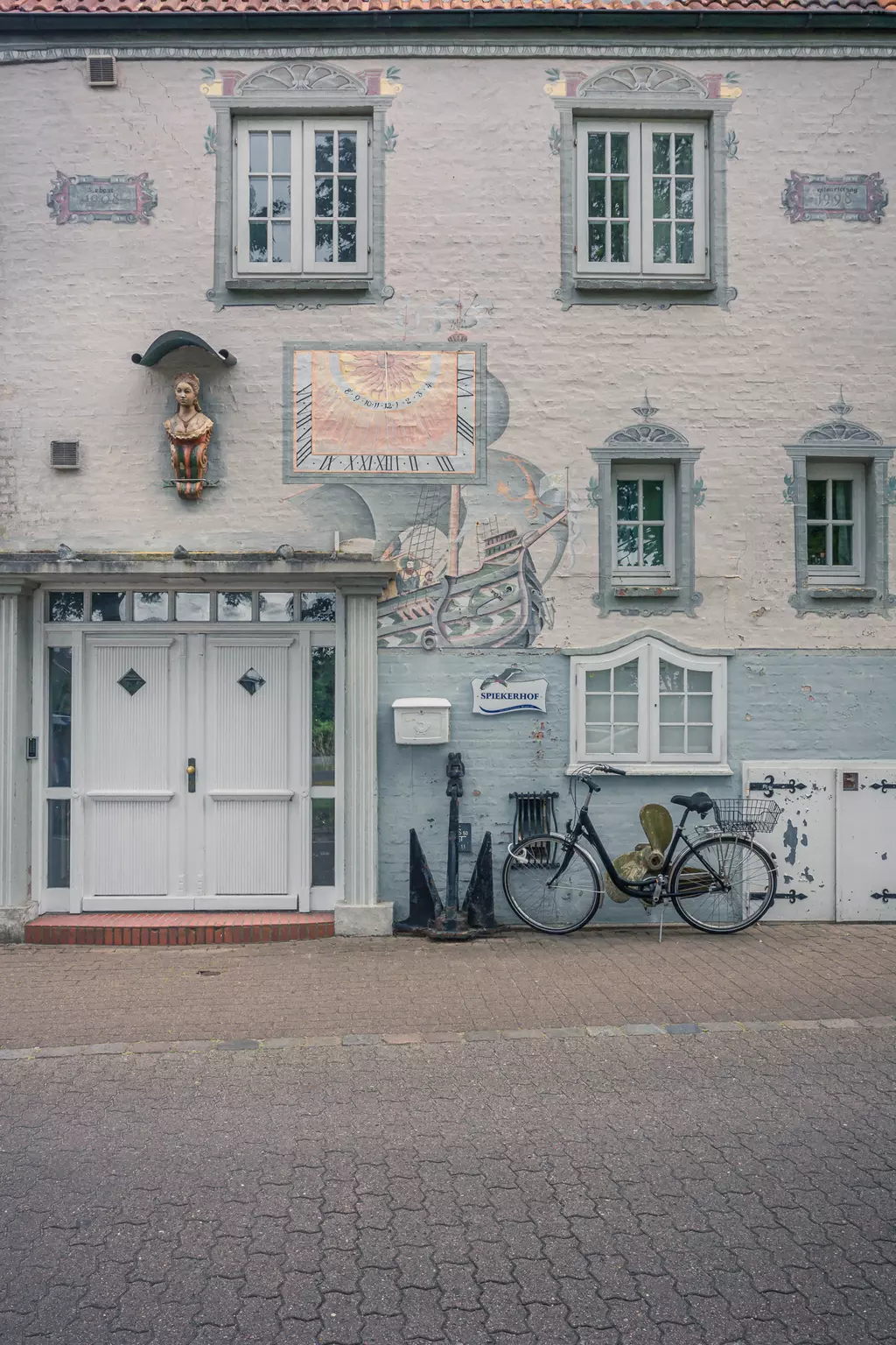 Hausfassade auf Föhr: Ein schmuckvolles Gebäude mit Fenster und Malereien, daneben ein altes Fahrrad und maritime Dekoration.