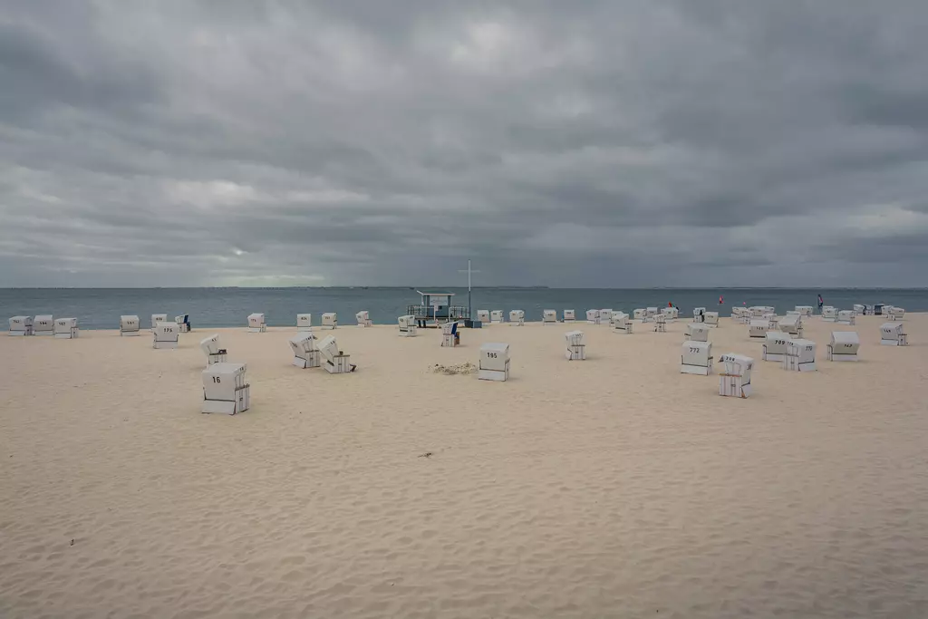 Strand auf Sylt: Zahlreiche Strandkörbe stehen auf hellem Sand, das Meer im Hintergrund, bewölkter Himmel.