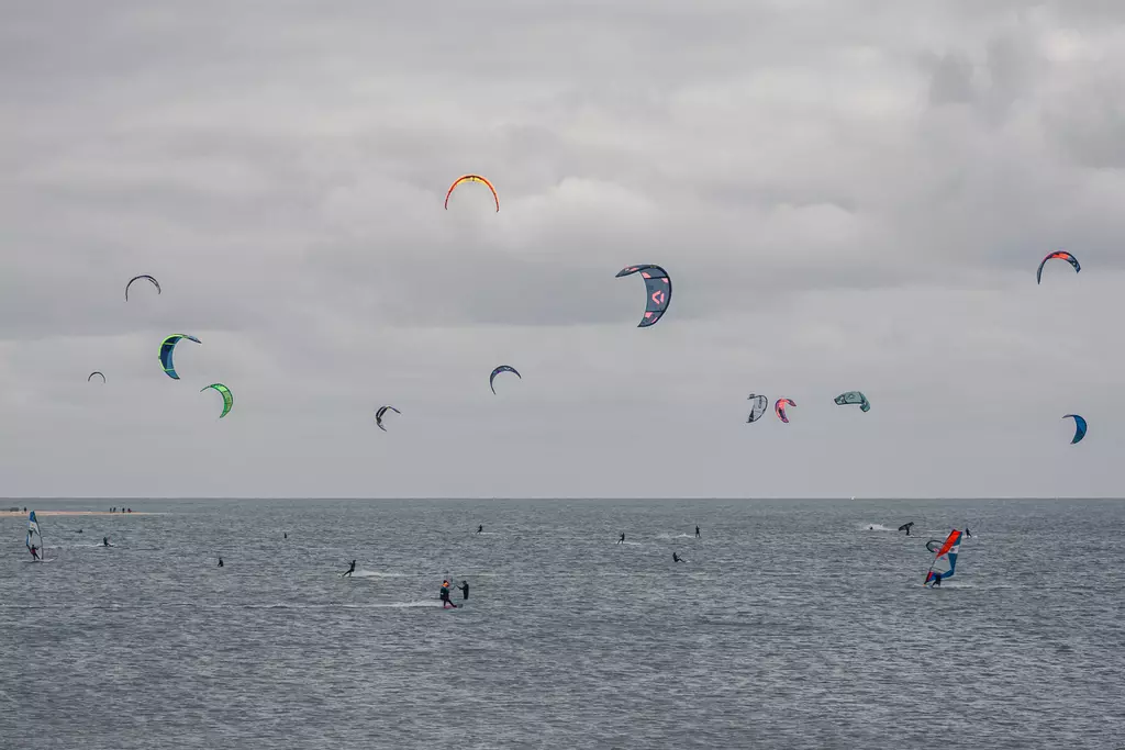 Kitesurfen auf Sylt: Viele bunte Kites schweben über einem grauen Meer, während Sportler auf dem Wasser unterwegs sind.