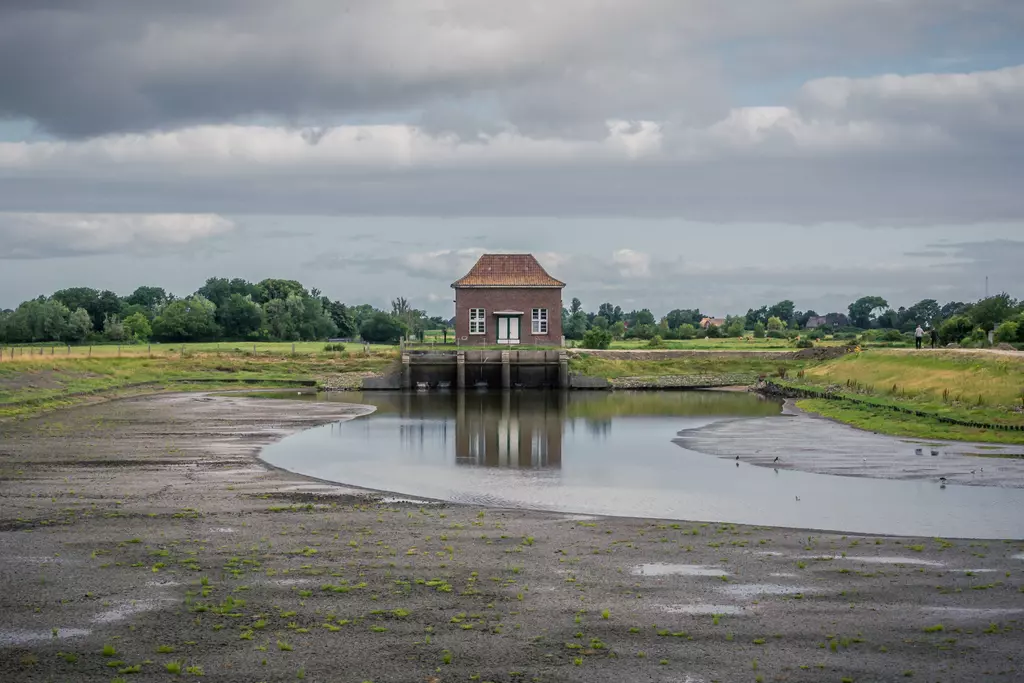 Ein kleines, rotes Gebäude steht in einer flachen, mit Wasser gefüllten Bucht in einer weitläufigen, grünen Landschaft.