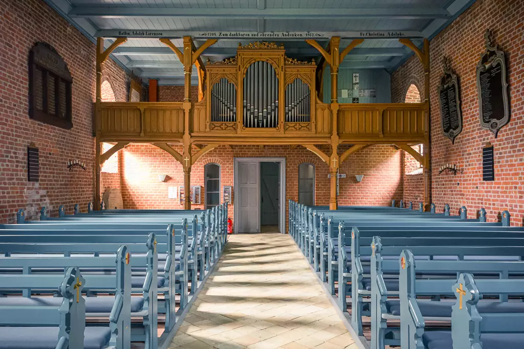 Blick in eine helle, ansprechend gestaltete Kirche mit Holzveranda, Orgel und blauen Bänken in symmetrischer Anordnung.