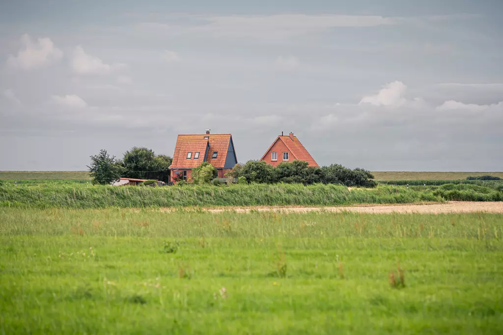 Zwei rote Häuser mit Satteldächern stehen umgeben von grünem Gras und Bäumen in einer weitläufigen Landschaft.