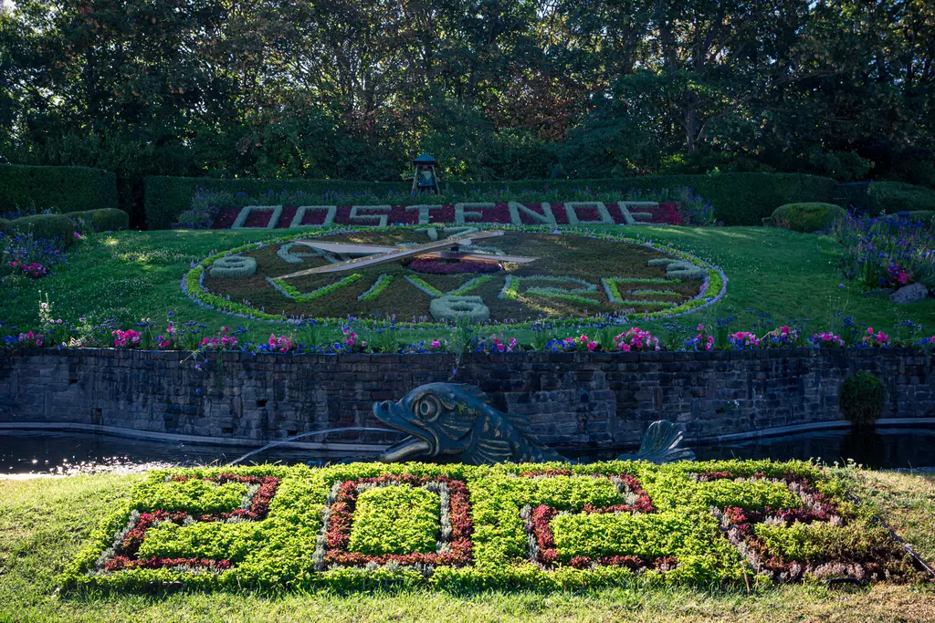 A colorful flowerbed with the number 2022 in the foreground and a large compass design behind, surrounded by green bushes.