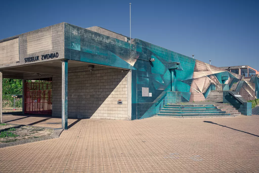 A modern swimming pool building with a colorful mural and a staircase on the side, surrounded by an open area.