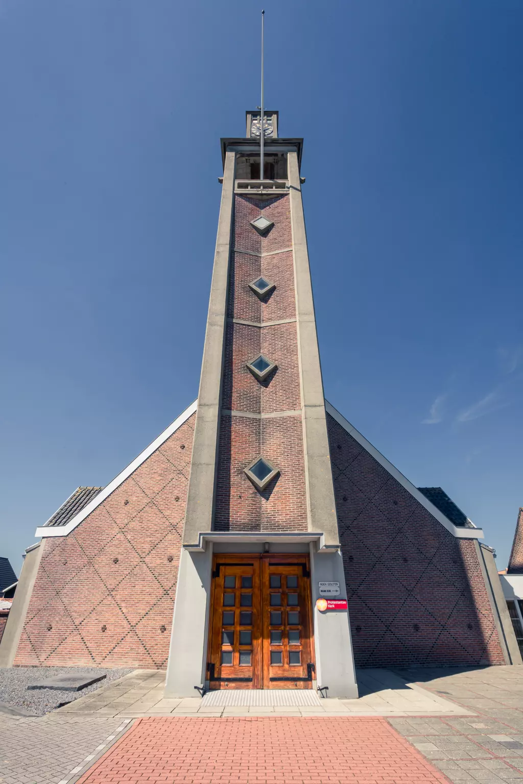 A modern hexagonal church with a trapezoidal facade and large wooden doors, set against a blue sky.