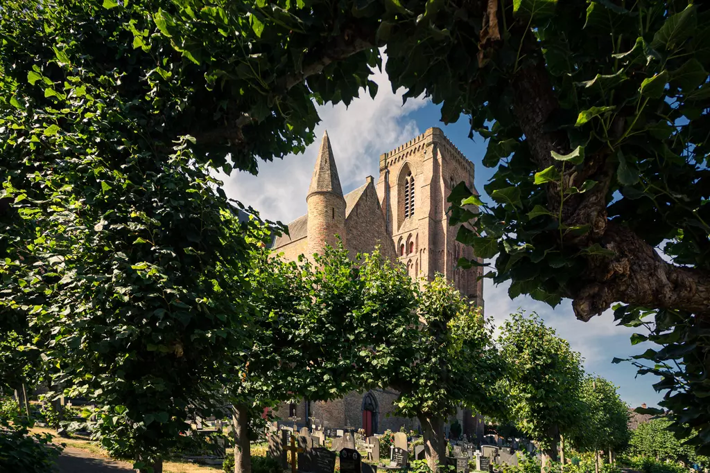 Eine historische Kirche ist von grünen Bäumen umgeben, mit steilem Dach und Türmen, unter blauem Himmel sichtbar.