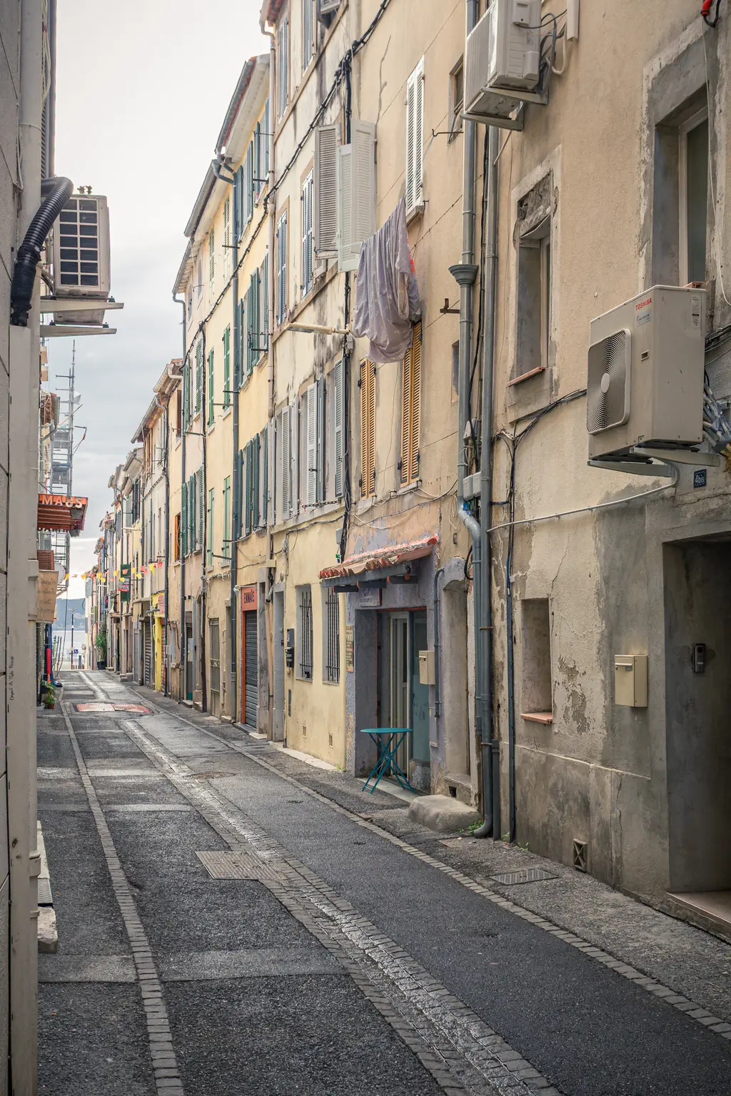 A narrow street in La Ciotat featuring tall, weathered buildings, colorful shutters, and a quiet atmosphere.