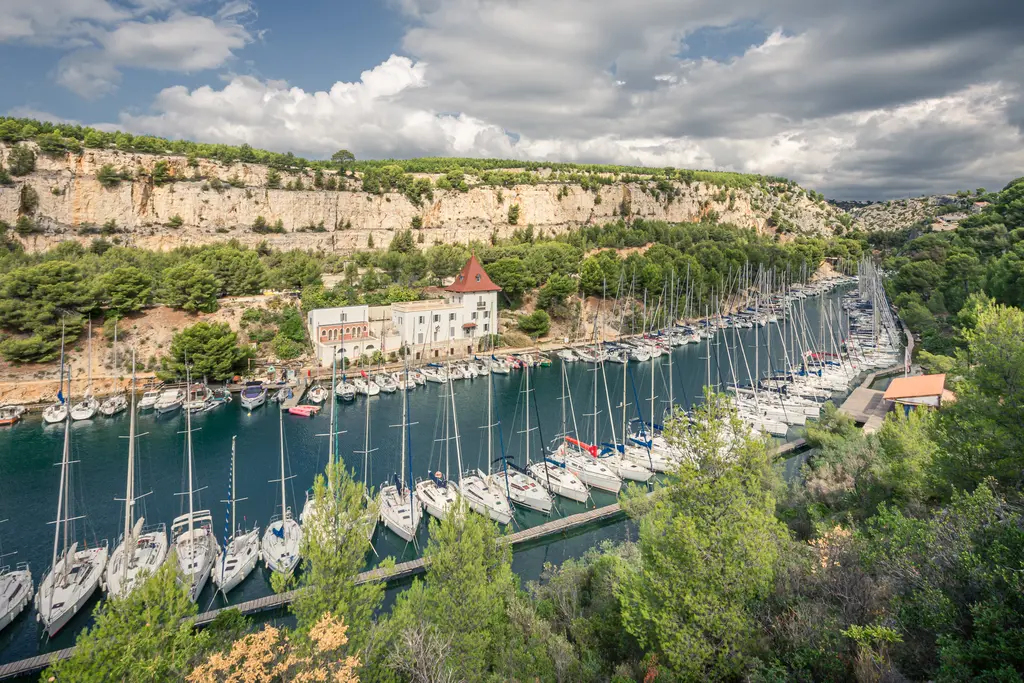 Marina in Calanque de Port-Miou bei Cassis, umgeben von hohen Felsen und saftigem Grün. Zahlreiche Segelboote liegen im ruhigen Wasser.