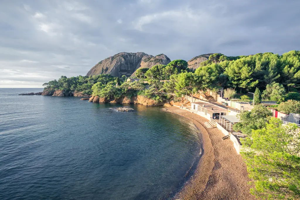A scenic view of La Ciotat's coastline featuring rocky cliffs, a pebbled beach, and lush greenery along the calm waters.