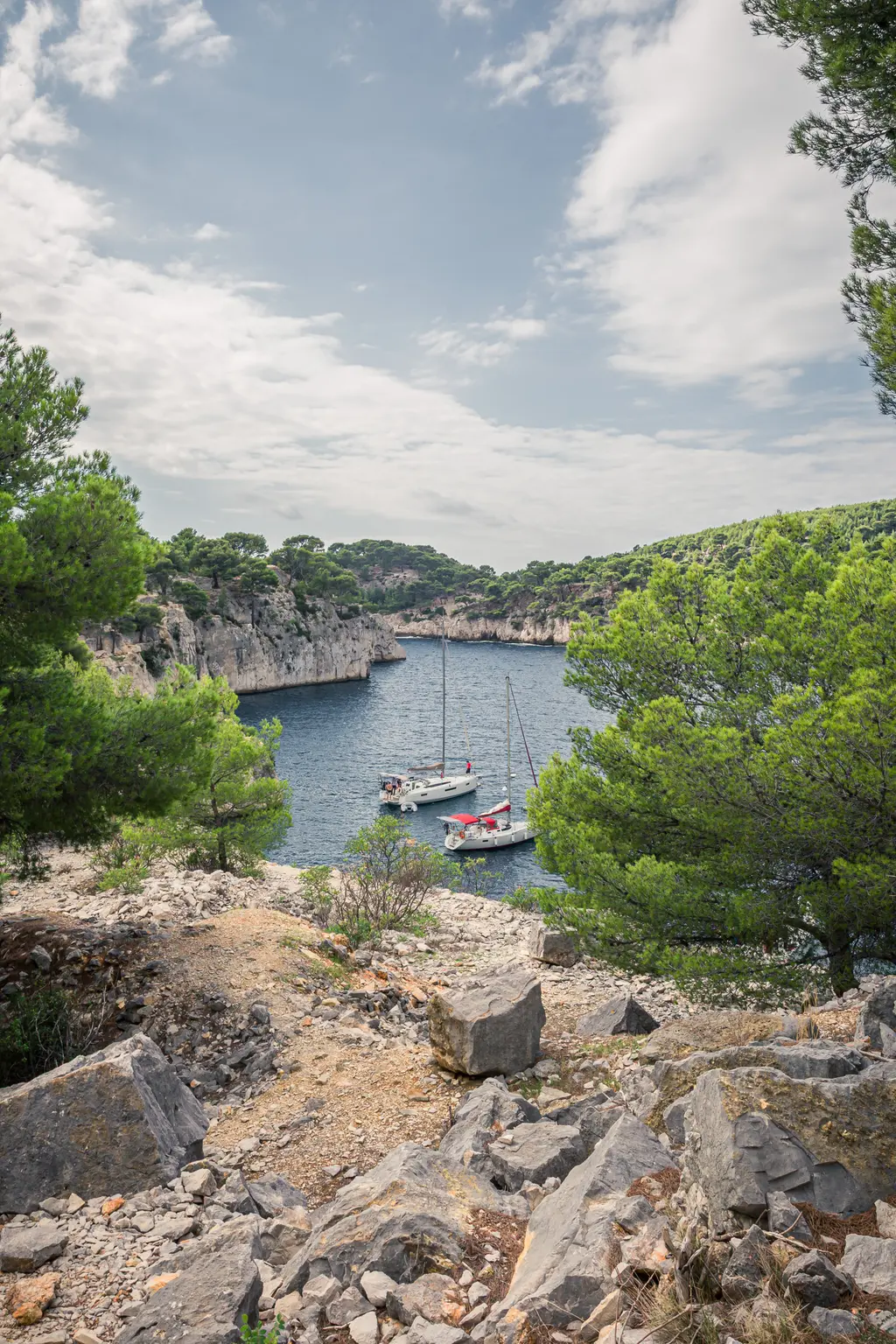 Blick auf die Calanque von Port-Miou in Cassis. Zwei Segelboote liegen ruhig im Wasser, umgeben von felsigen Klippen und dichten Bäumen.