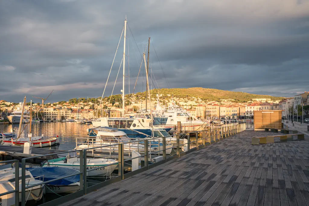 A picturesque harbor in La Ciotat with boats and a scenic waterfront, bathed in golden light under a dramatic sky.