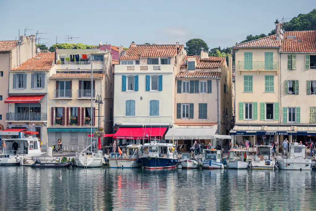 Hafenansicht in Cassis mit bunten Häusern und anlegenden Booten. Die Gebäude haben rote Ziegeldächer und grün gestrichene Fenster.