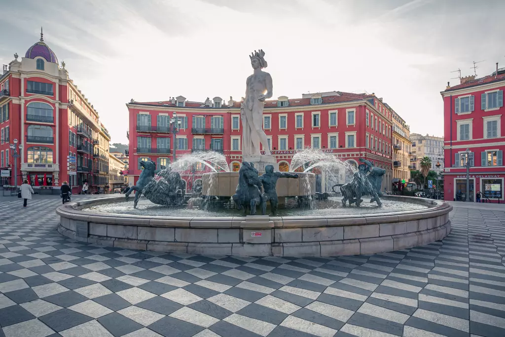 Fontaine du Soleil in Nice: Fountain with a central statue, surrounded by water sprays and colorful buildings in the background.